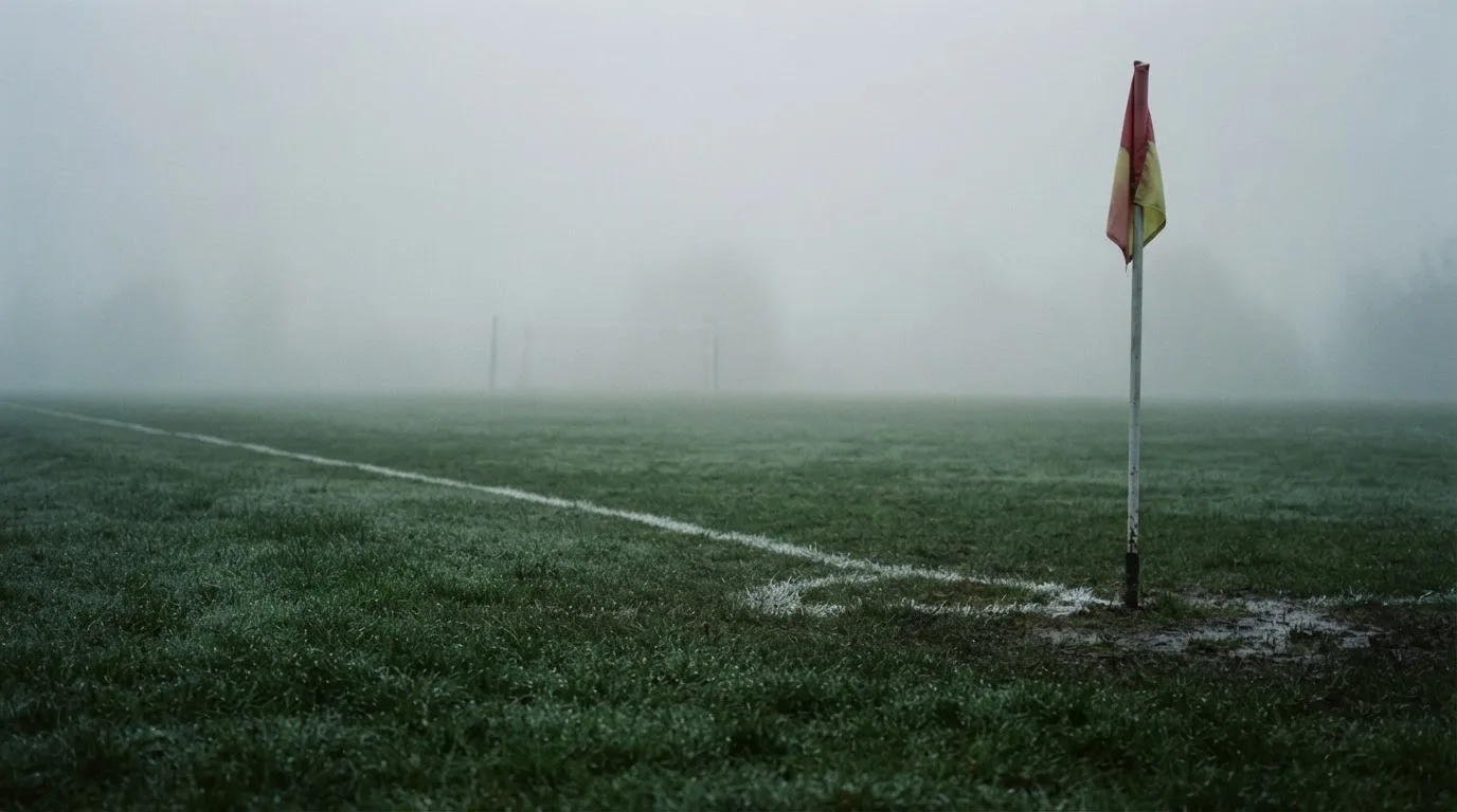 Der Rand eines Spielfelds mit weißer Linie und Eckfahne bei Nebel am frühen Morgen, ohne Menschen.