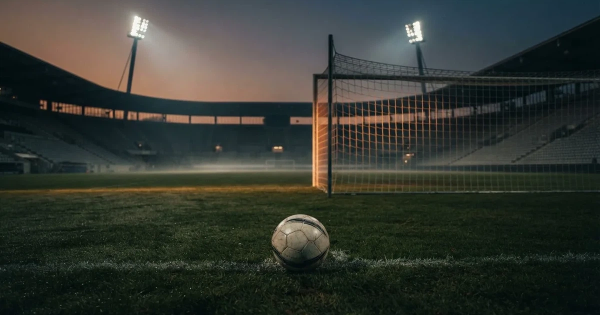 Ein Fußball liegt im Strafraum direkt vor dem Tor mit Netz, im Hintergrund leere Ränge bei Dämmerung.