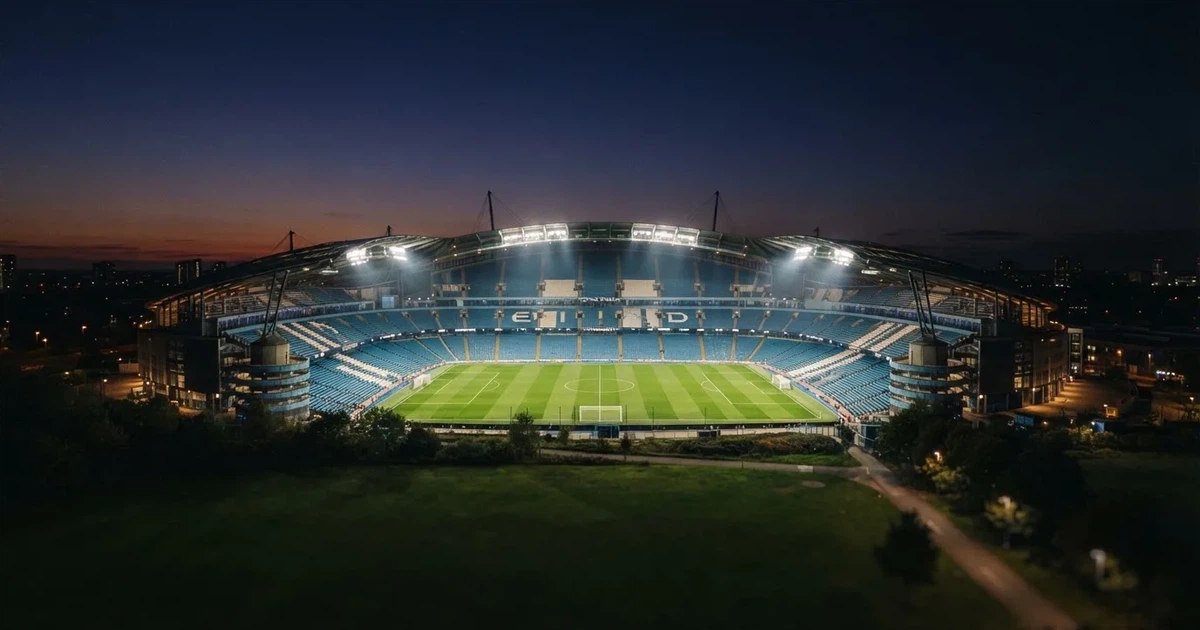Ein großes Stadion bei Nacht, aus der Ferne unter Flutlicht gesehen, die Ränge hell erleuchtet, der Rasen leuchtend grün.