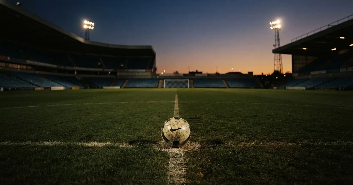 Ein Fußball liegt auf dem Rasen eines leeren Stadions bei Flutlicht, im Hintergrund unscharfe Tribünen ohne erkennbare Beschriftung.