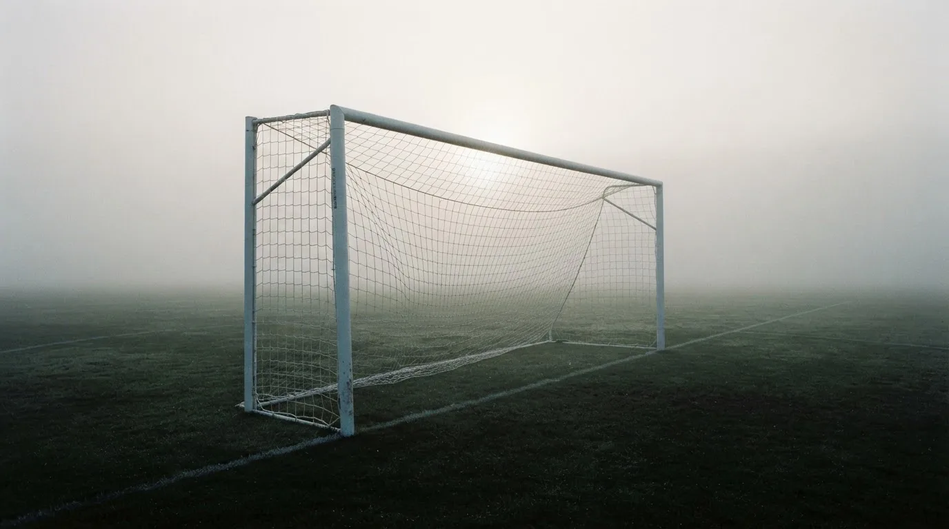 Ein Fußballtor mit Netz im Morgennebel auf einem leeren Platz, die Linien nur schwach zu erkennen.