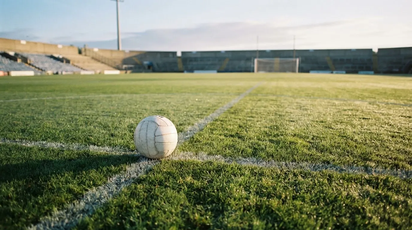 Ein Fußball liegt auf dem Anstoßkreis eines leeren Rasenplatzes im frühen Morgenlicht.
