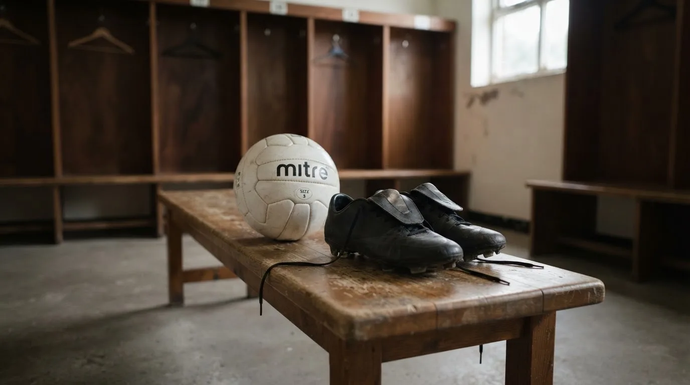Ein Fußball liegt neben einem Paar Fußballschuhen ohne Markenzeichen auf einer Holzbank in einer leeren Umkleide.