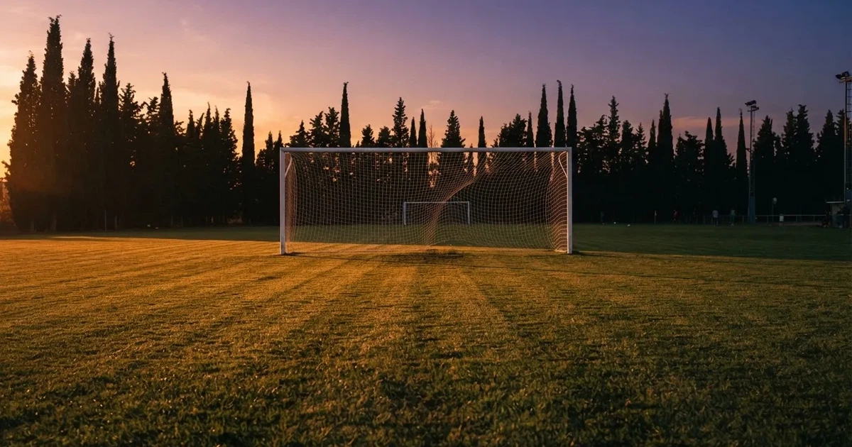 Ein Fußballtor mit Netz auf einem leeren Platz im Abendlicht, der Rasen frisch gemäht, im Hintergrund Zypressen.