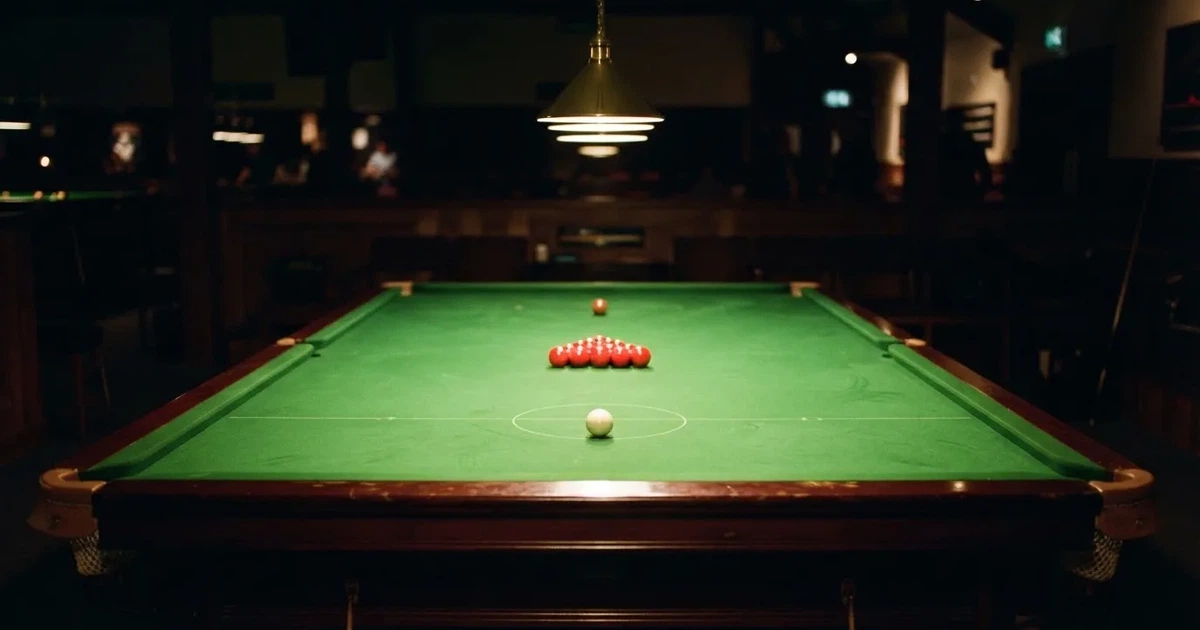 Ein Snookertisch mit grünem Tuch und aufgebauten roten Kugeln in einem abgedunkelten Raum unter einer hängenden Lampe.