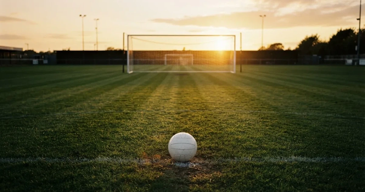 Ein Fußballtor mit Netz im Gegenlicht auf einem leeren Platz am Abend, davor ein Ball auf dem Rasen.