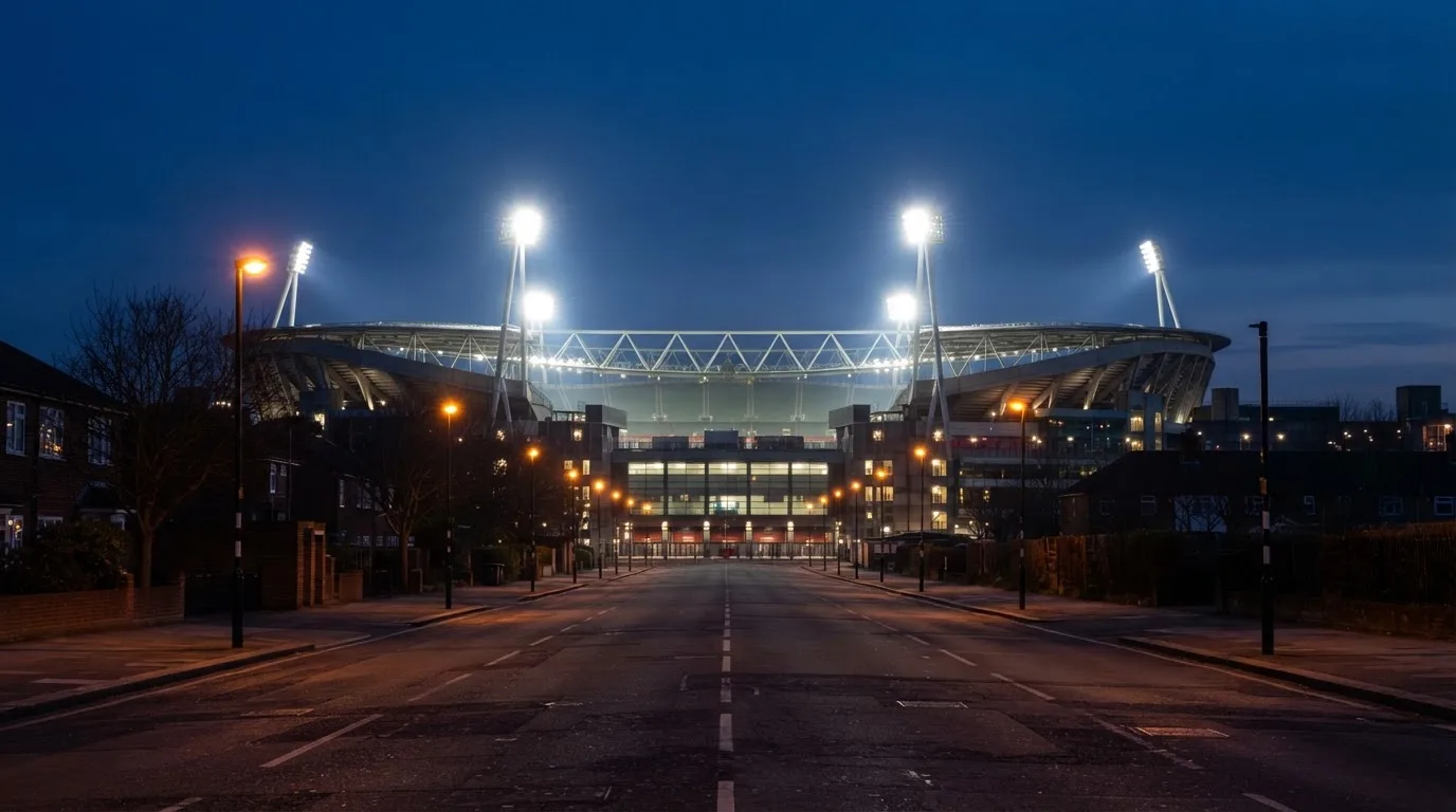 Ein Stadion unter Flutlicht aus großer Entfernung, davor eine leere Straße in der Abenddämmerung.
