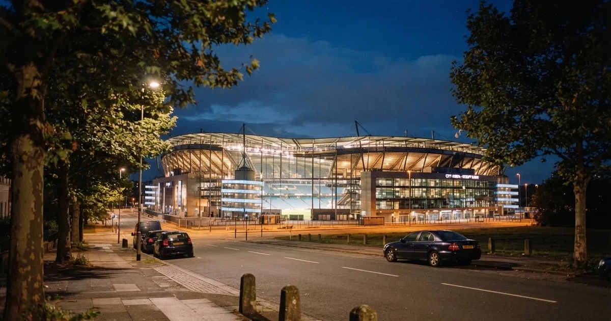 Ein hell erleuchtetes Stadion aus der Ferne bei Nacht, davor eine stille Straße und ein paar Bäume.