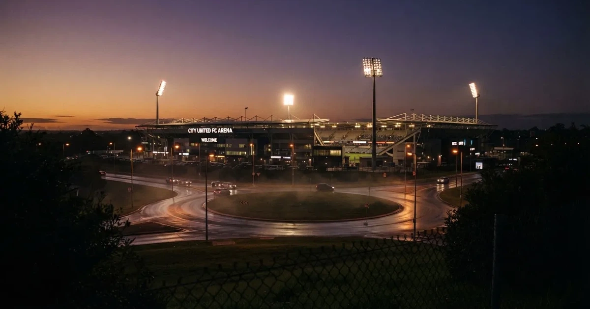 Ein Fußballstadion in der Dämmerung aus der Ferne, die Flutlichter gerade eingeschaltet, davor ein Kreisverkehr mit Laternen.